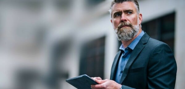 A bearded man looking at a building with a clipboard in his hand