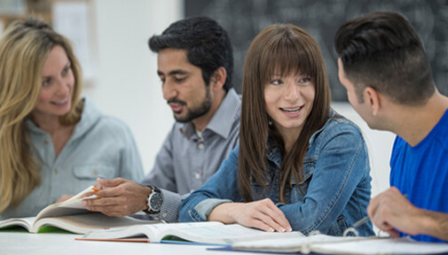 Students with their books open on a desk, chatting to each other